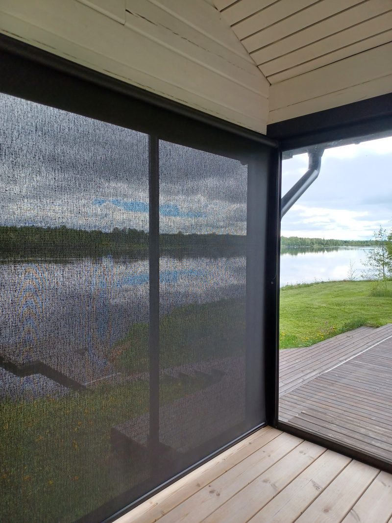 Läpinäkyvä screen-rullaverho katetun terassin aukossa, taustalla järvi