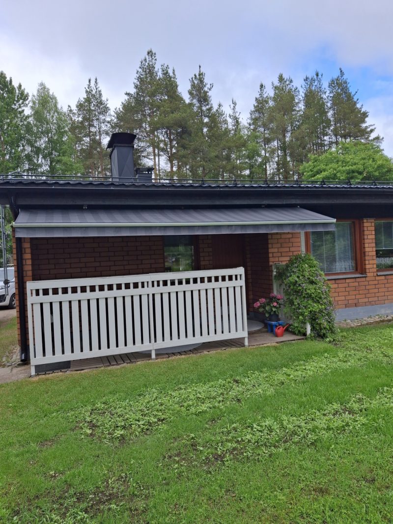 Tummanharmaa terassimarkiisi tiilitalon terassin yllä, edessä valkoinen terassiaita